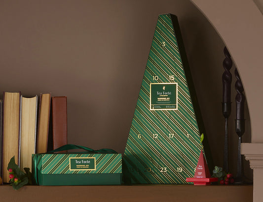 MAIN PDP | A green triangular Advent Calendar with diagonal striped pattern and gold numbers, displayed on a shelf next to a smaller matching box and decorative items.