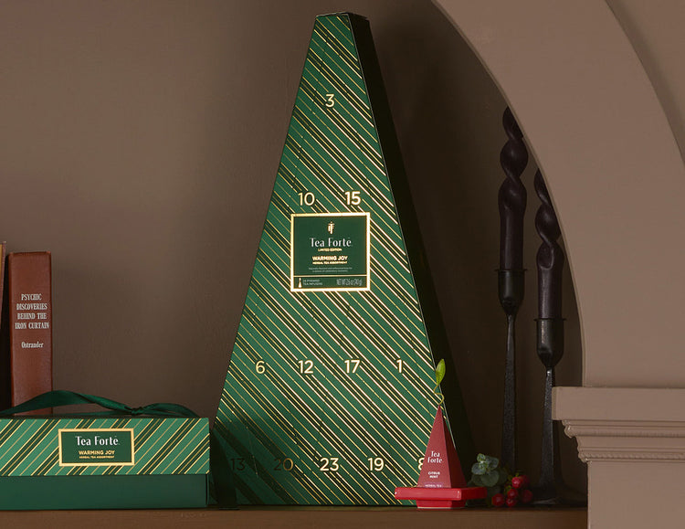 A green triangular Advent Calendar with diagonal striped pattern and gold numbers, displayed on a shelf next to a smaller matching box and decorative items.