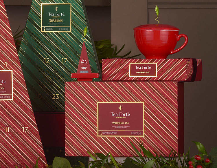 MAIN PDP | Warming Joy Gift Set styled with a red teacup and Petite BBox and Tea Tray  along with other red and green striped boxes  against a background with holiday greenery.