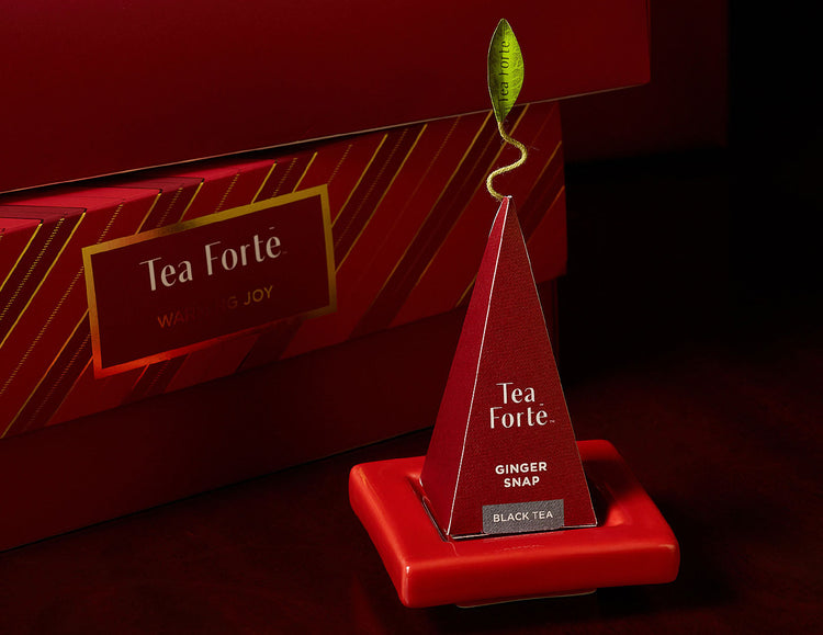 A red pyramid-shaped tea infuser on on a red Tea Tray, with a matching Petite Presentation Box in the background.