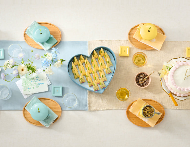 Keepsake Heart Box, Something Blue, of 26 pyramid infusers, lid open, revealing infusers, with cups of tea on a table with shower and birthday items