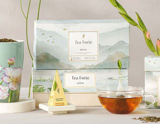 Lotus Petite Presentation Box of 10 pyramid infusers, 2 boxes stacked on top of another, with teacups ad flowers around, and infuser on white tray in front