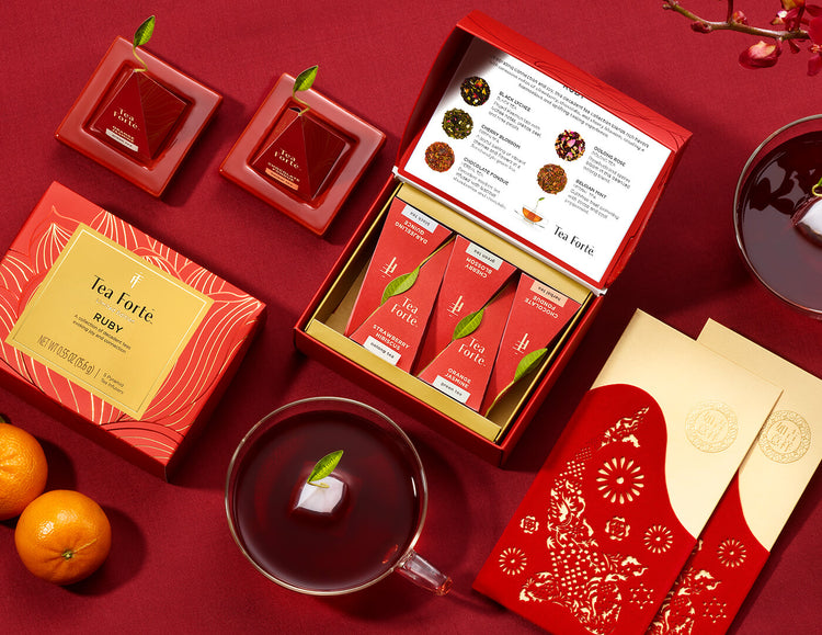 Ruby Mini Petite Box of 5 teas, open and closed on a table with cups of tea and red envelopes, tangerines, and teas on Ruby Red Tea Trays