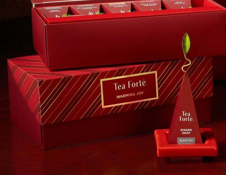 Presentation Box Warming Joy, of 20 tea infusers, open and closed, with a Tea Tray and pyramid infuser on it out front.