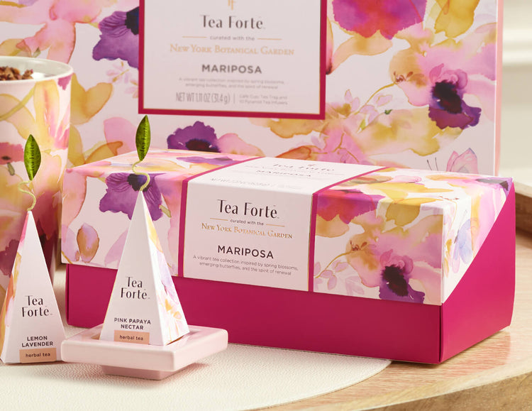 MAIN PDP | Mariposa Presentation Box of 20 pyramid tea infusers,  closed box o a table with a glass cup of tea and other boxes and infusers