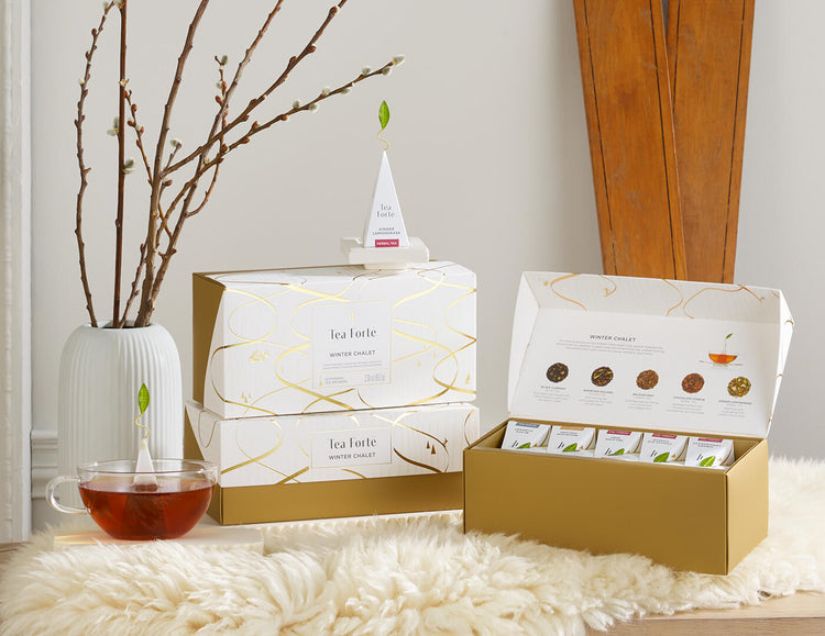 Presentation Boxes of Winter Chalet, one open, two closed, on a white fur throw with a white vase, glass teacup and wooden skis