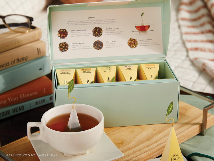Lotus Presentation Box of 20 pyramid tea infusers, lid open on a wooden tray with a white cup of tea